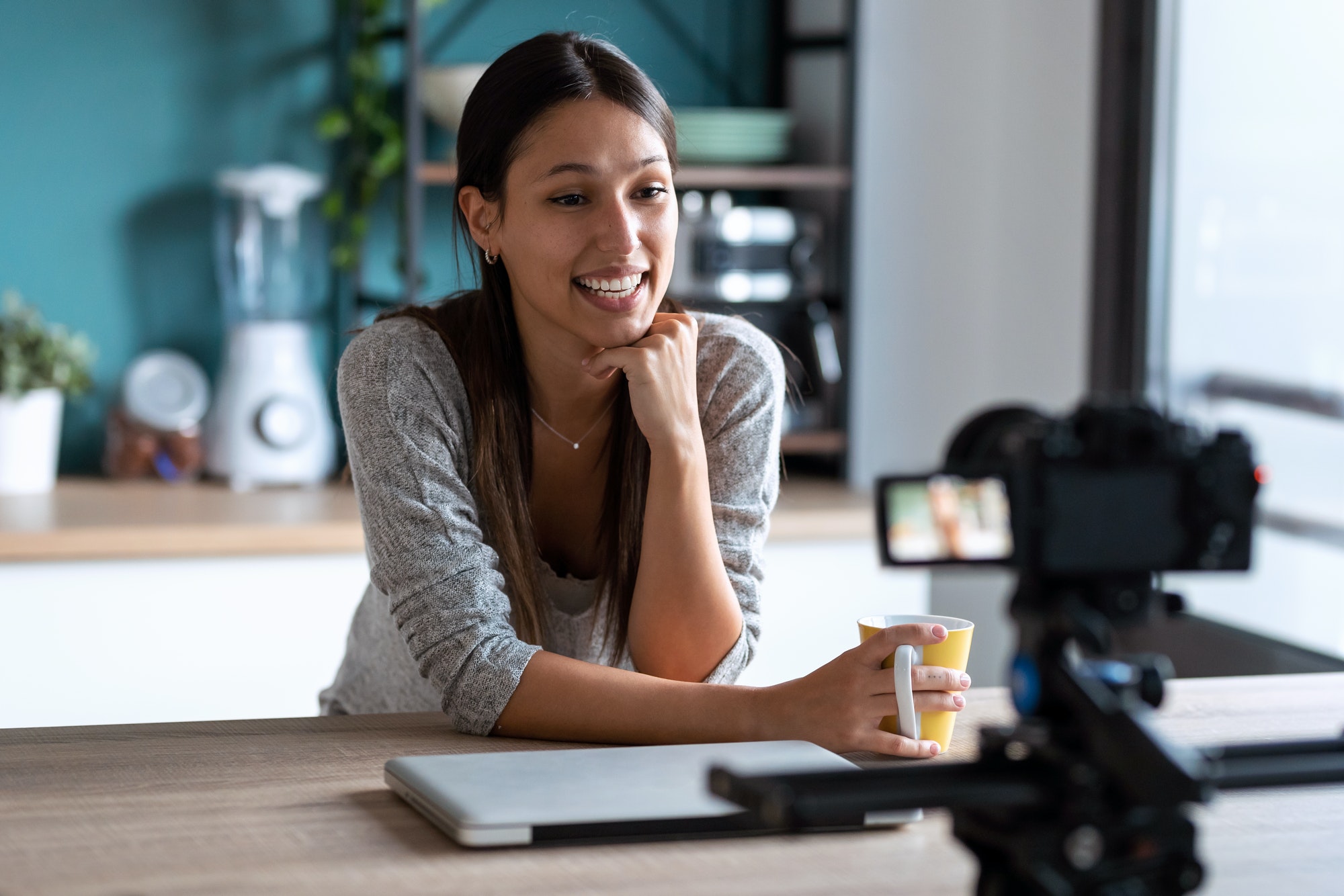 Smiling young woman doing a video blog with the camera in the kitchen.